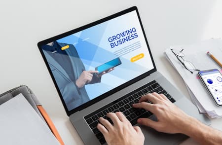 Dwie ręcę na klawiaturze laptopa z wyświetloną stroną biznesową